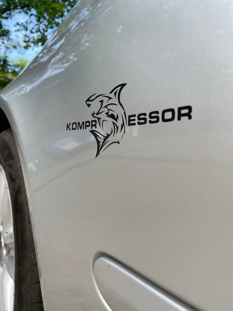 Close-up of white RV with black Kompressor fish logo and text on exterior side panel